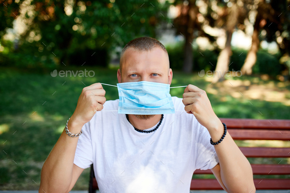 Portrait of man takes off protective mask in the park outdoor in the city - Stock Photo - Images