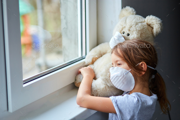 Little girl holding and hugging teddy bear in mask near the window. - Stock Photo - Images