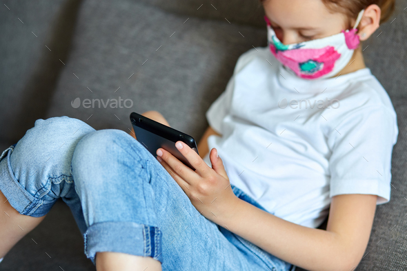 Little girl in protection mask using, play tablet or learning with video call online - Stock Photo - Images