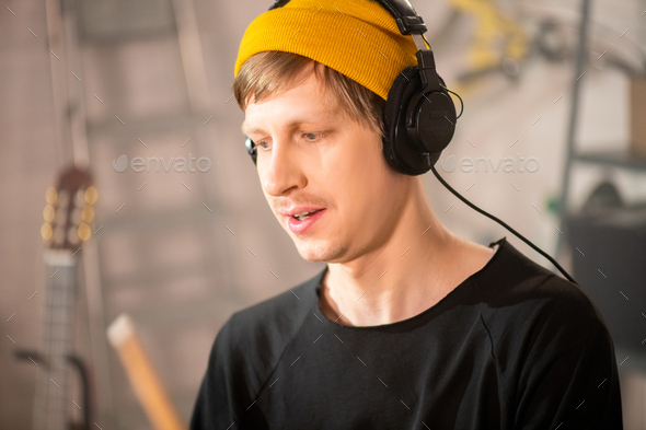 drummer in beanie and headphones recording new music in garage Stock by Pressmaster