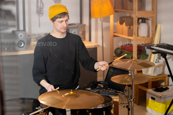 Contemporary musician beating cymbals with wooden drumsticks in garage