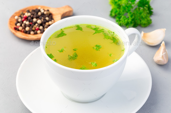 Chicken broth in white cup garnished with chopped parsley, vertical, horizontal