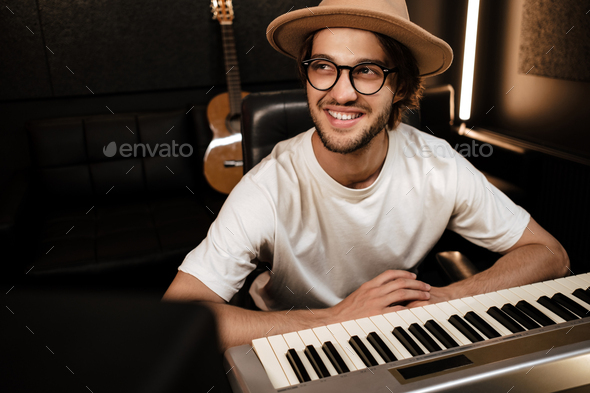 Young attractive stylish musician happily working in modern sound recording studio