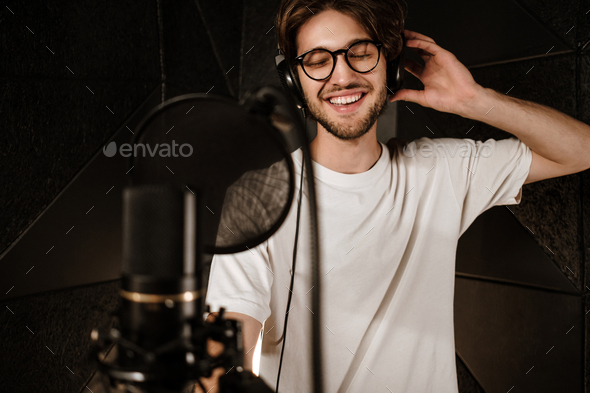Young attractive male singer in headphones joyfully singing in sound studio
