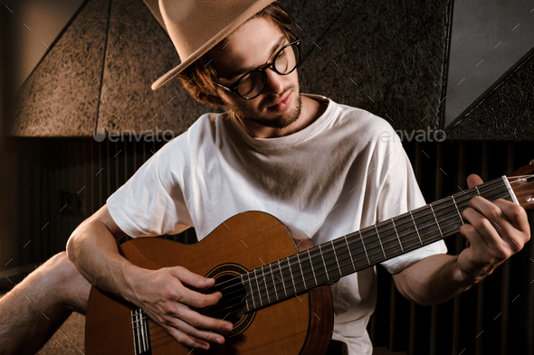 Portrait of attractive male musician intently playing on guitar in recording studio - Stock Photo - Images