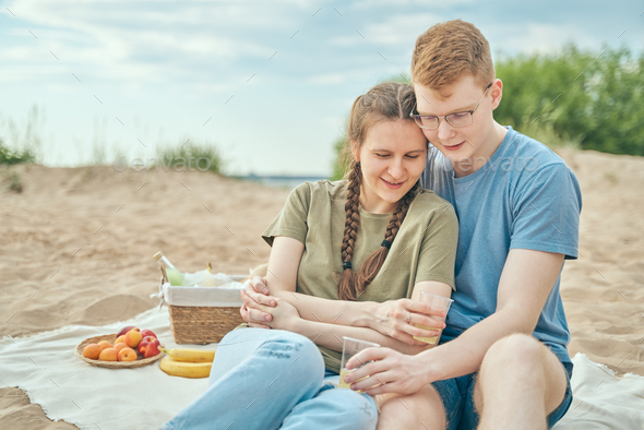 Young couple enjoying picnic on beach embracing and holding cups - Stock Photo - Images