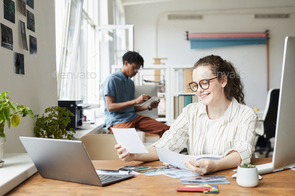 Smiling Young Woman Looking at Photos in Office