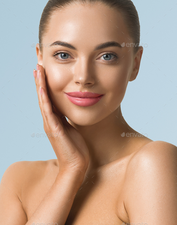 Clean skin woman face close up beauty tanned face beautiful smile. Blue background. Touching face.