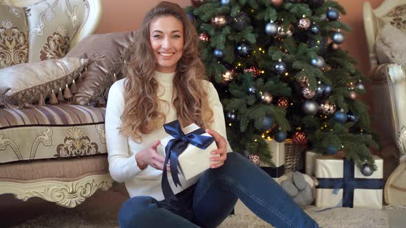 Christmas. Woman Dressed White Sweater and Jeans Sitting on the Floor Near Christmas Tree with alt