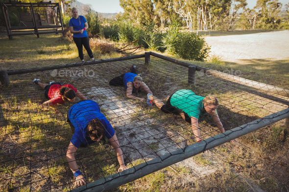 Group of fit women crawling under the net during obstacle course ...