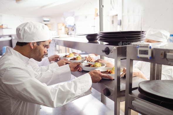 Chefs passing ready food to waiter at order station