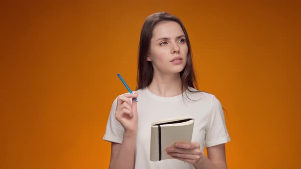 Thoughtful Young Woman Making Notes in Notepad Against Yellow Background alt