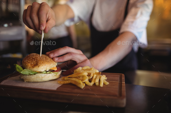 Chef placing tooth pick over burger at order station