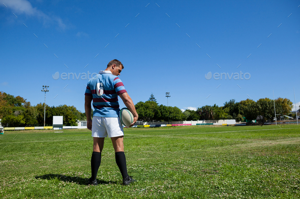 Rear view of rugby player holding ball at field