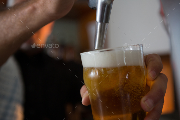 Brewer filling beer in beer glass from beer pump in bar