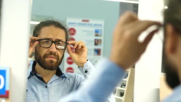 Bearded man is choosing eyesight glasses at optics store