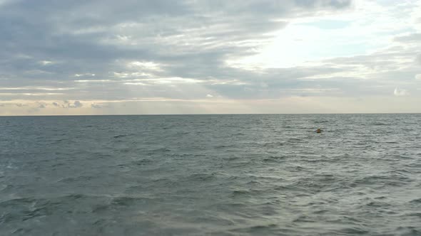 Yellow Buoy in Rough Ocean with Sunset Cloudscape in Distance, Aerial Forward alt