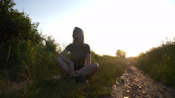 Blonde woman is sitting at countryside road in sunset time