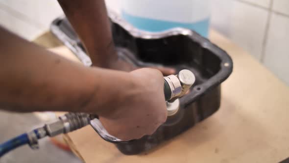Mechanic removes gasket from car oil sump using wire brush on rotary device alt