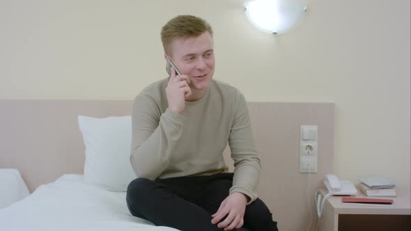 Man Talking and Laughing on His Smartphone Seated on a Bed alt