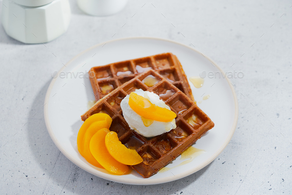 Sweet Homemade Belgian Waffle with honey, peaches in syrup, whipped cream in plate.