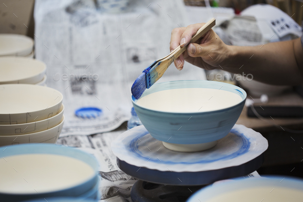 Close up of person working in a Japanese porcelain workshop, painting white bowls with blue glaze.
