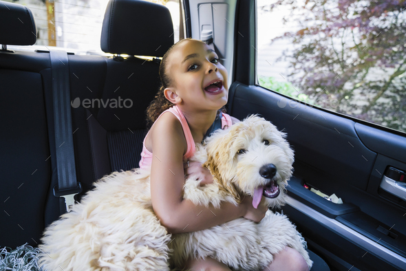 Girl with labradoodle puppy in car making goofy face