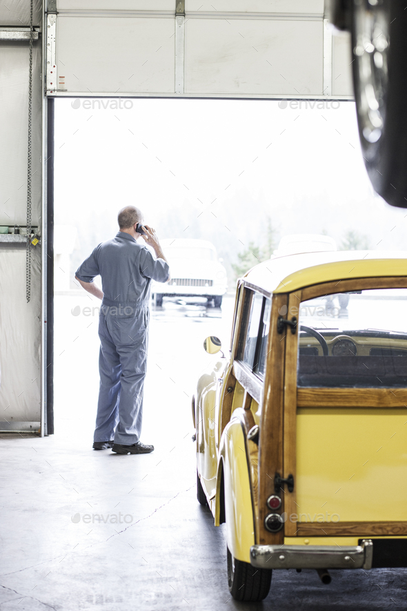 View from behind of an owner of a car repair shop on his cell phone.