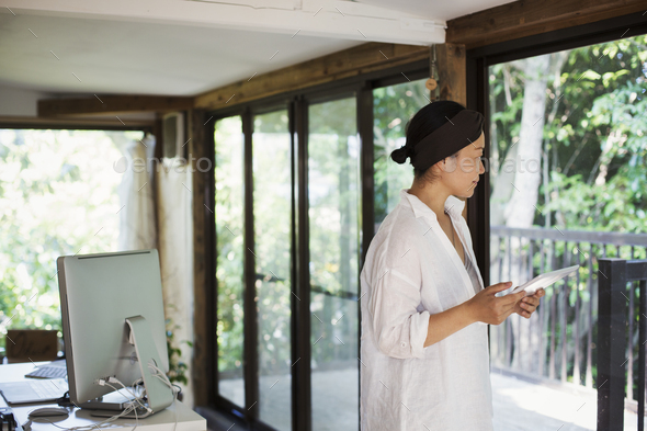 Woman standing indoors behind desk with computer monitor, holding ...