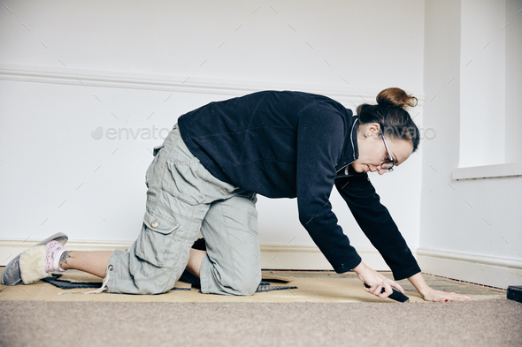 Woman using knife to cut away carpet on floor