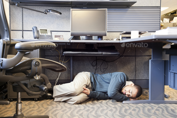 A Black man taking a nap under his desk in a corporate office