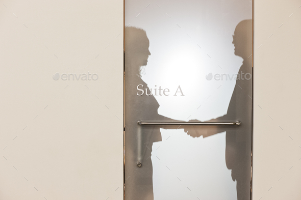 Two business people shaking hands and silhouetted through the frosted glass door of an office suite