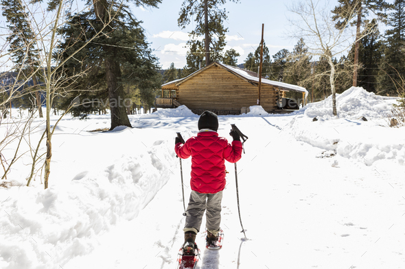 Rear view of young boy in a red jacket snow shoeing
