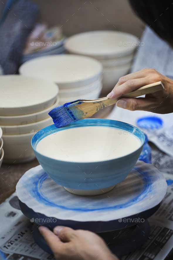 Close up of person working in a Japanese porcelain workshop, painting white bowls with blue glaze.