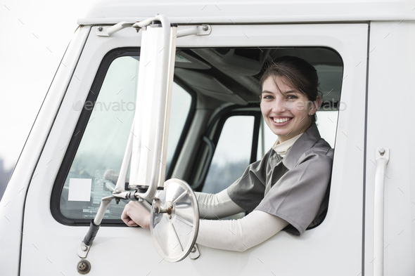 Portrait of a caucasian female truck driver in the window of her truck at a distrubiton warehouse.