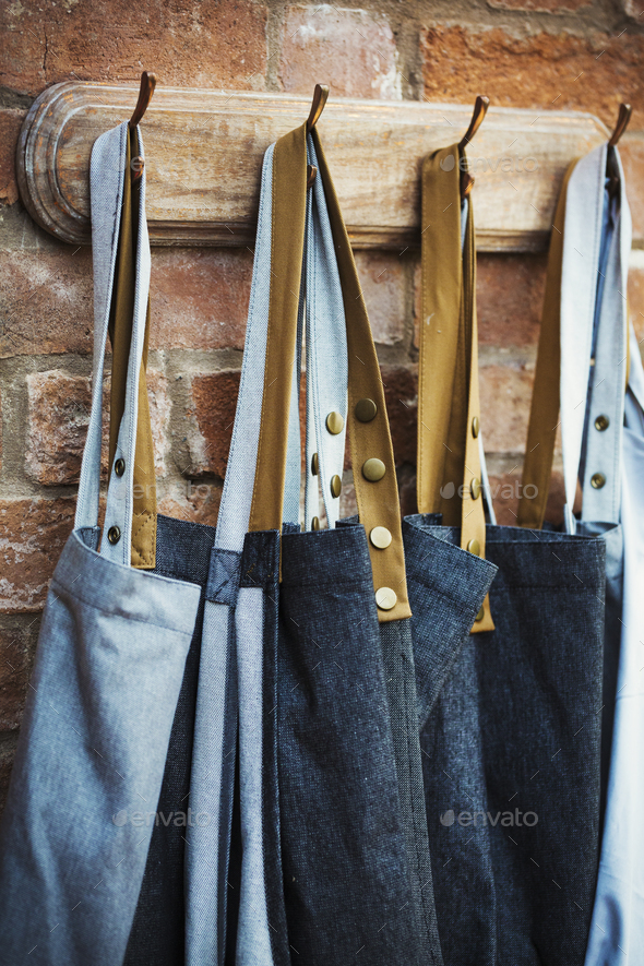 Denim work aprons hanging on a row of hooks on a brick wall. Stock Photo by  Mint_Images