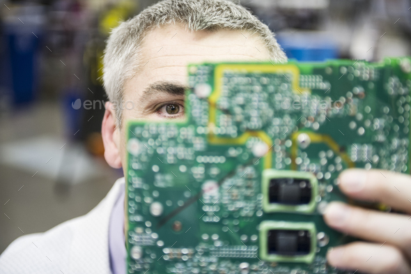 A caucasian male technician examinging a circuit board in a technical research and development site.
