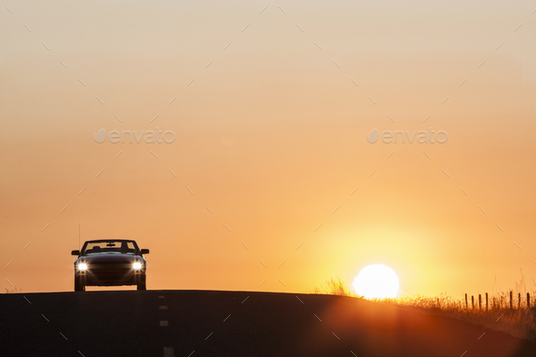 A convertible sports car on a country highway at sunset.