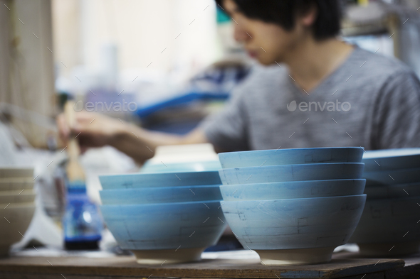 Close up of man working in a Japanese porcelain workshop, painting white bowls with blue glaze.