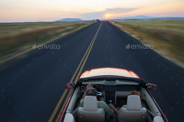 Senior couple in a convertible sports car driving on a highway at sunset