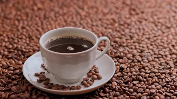 Black Coffee in a White Cup with Spinning Bubbles on a Flat Surface Covered with Roasted Coffee