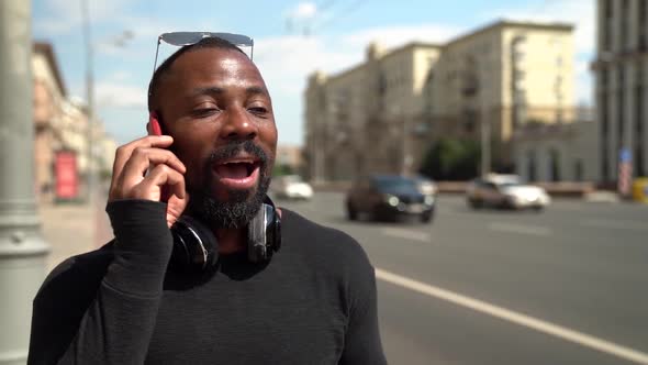 Portrait of an African Man with Glasses on Forehead and Headphones Around Neck. He Talks on the Red alt