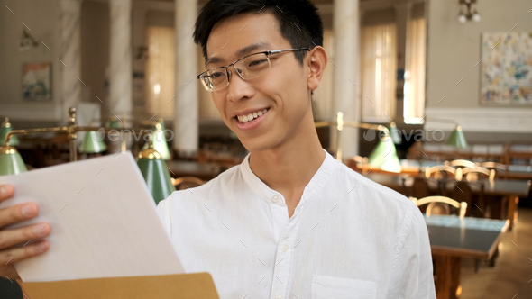 Portrait of asian student happily opening envelope with exam results in university library
