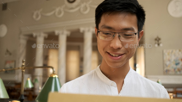 Portrait of smiling asian student happily opening envelope with exam results in university library