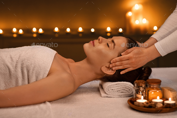 Relaxed young woman getting head massage at romantic spa atmosphere