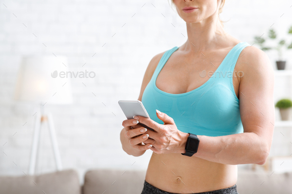 Fitness trainer remotely at home. Muscular woman with smart watch looks at phone