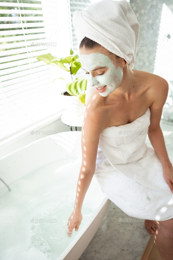 Woman with face pack with her hand in the bathtub