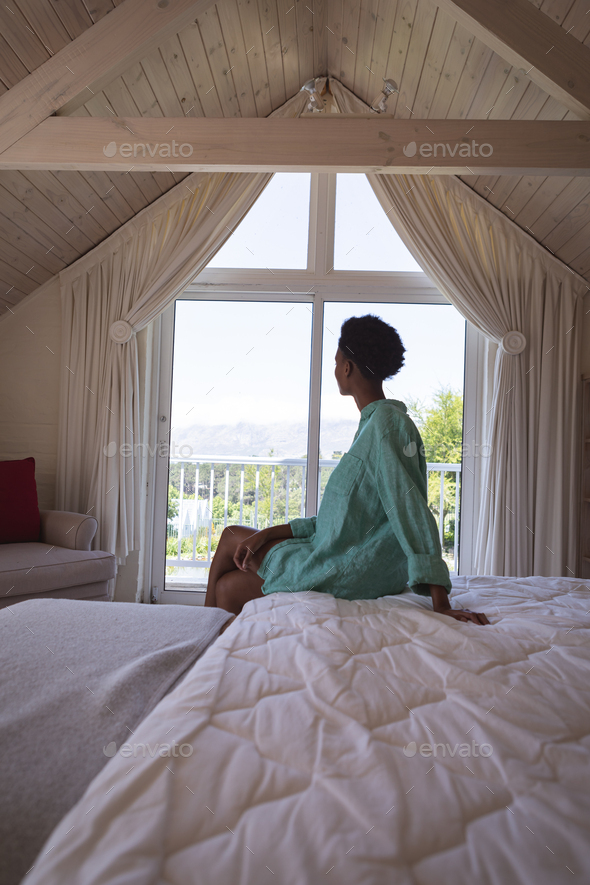 Woman looking out of the window while sitting on her bed