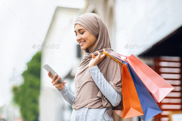 Happy arab woman with shopping bags using smartphone