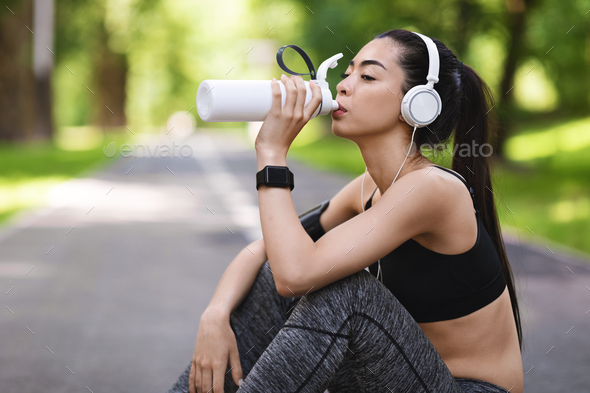 Thirsty After Training. Young asian girl drinking water, resting after jogging outsoors